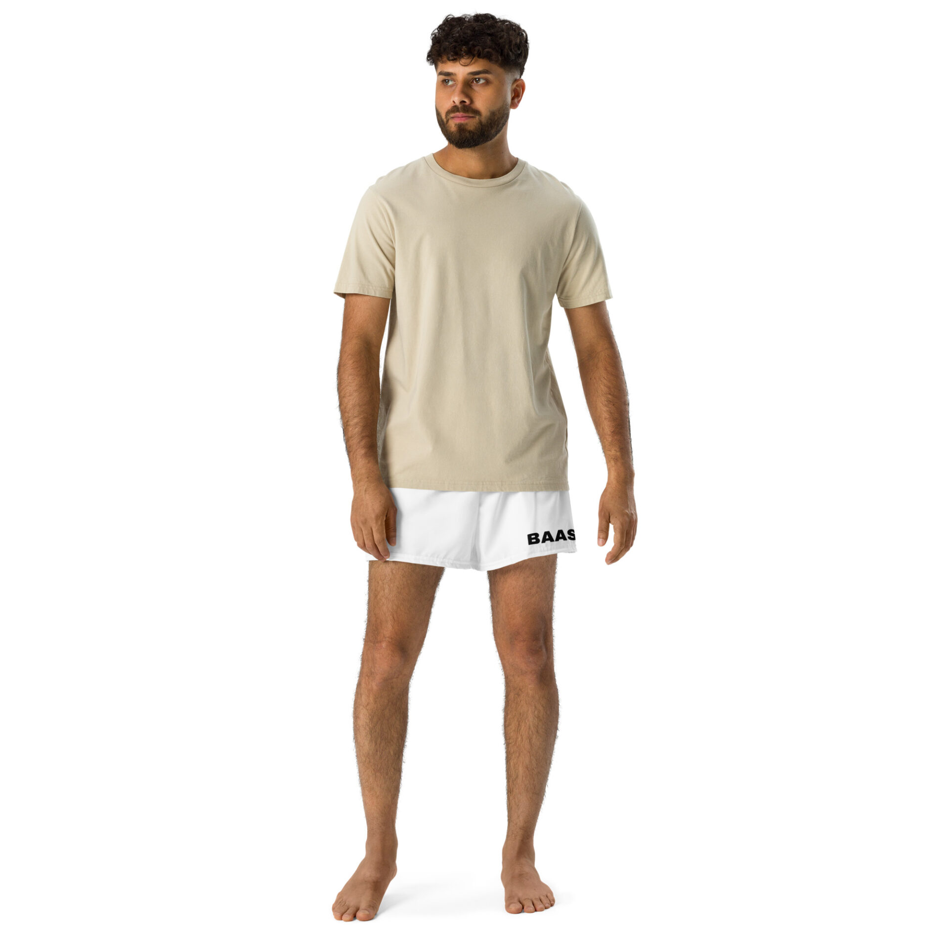 A curly-haired, bearded man stands barefoot on a white backdrop, wearing a beige t-shirt and stylish BAAS Athletic Shorts with BAAS printed on the leg.