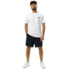 A man with curly hair and a beard stands against a white background, wearing an Under ArmourⓇ athletic t-shirt with BAAS. on the chest, black shorts, and white sneakers, hands by his sides.