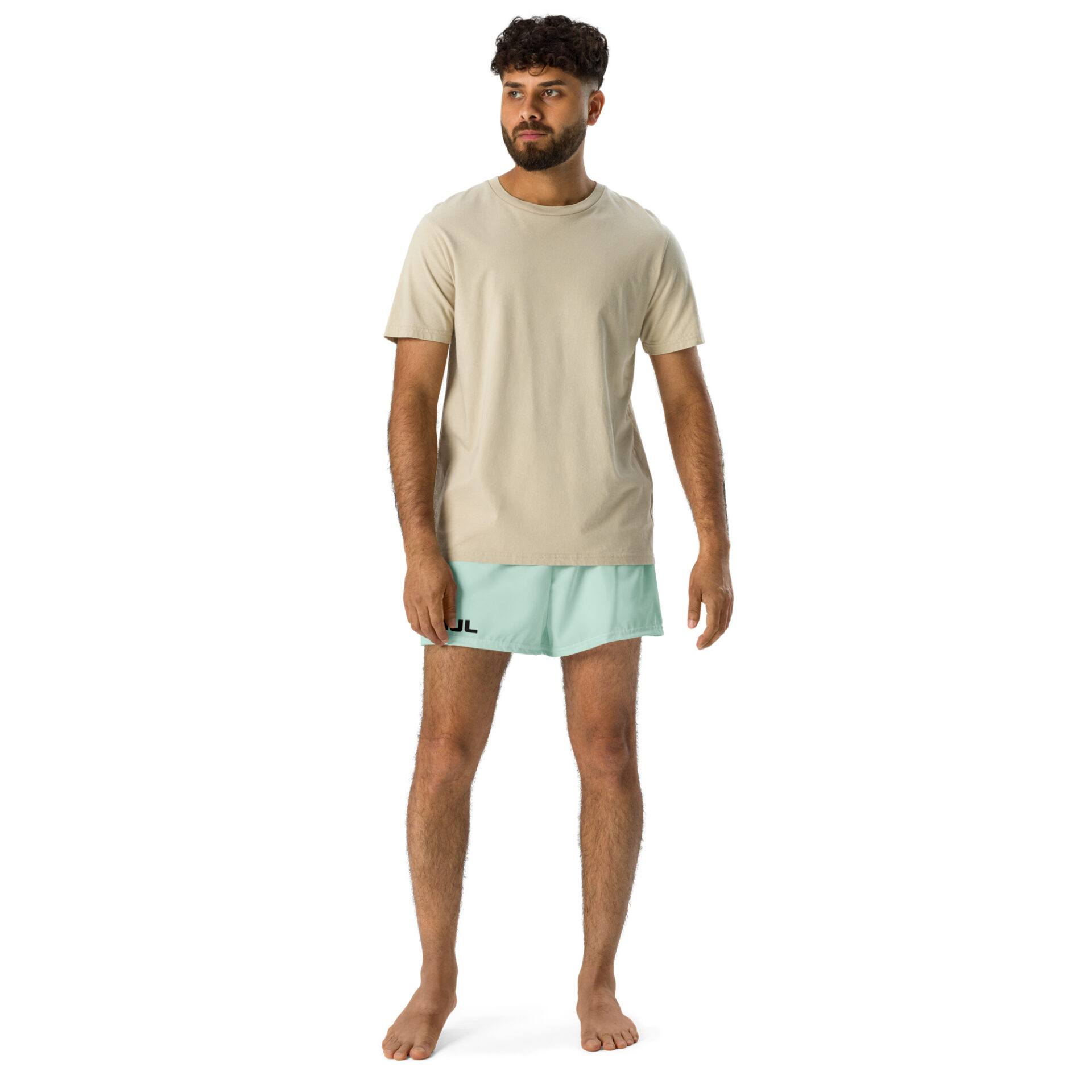 A barefoot man with short curly hair and a beard wears a beige T-shirt and light blue MJL Athletic Shorts featuring a black logo on the left leg, posed against a plain white background.