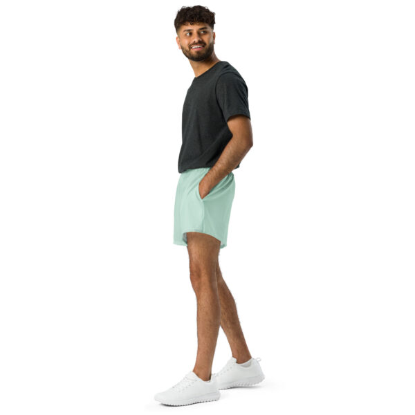 A man stands sideways with one hand in his pocket, wearing a dark t-shirt, MJL Athletic Shorts in light green, and white sneakers, set against a plain white background.