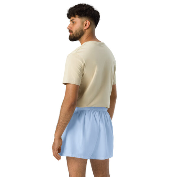 A man with short dark hair and a beard, wearing a beige T-shirt and light blue MJL Athletic Shorts, stands facing away against a plain white background.