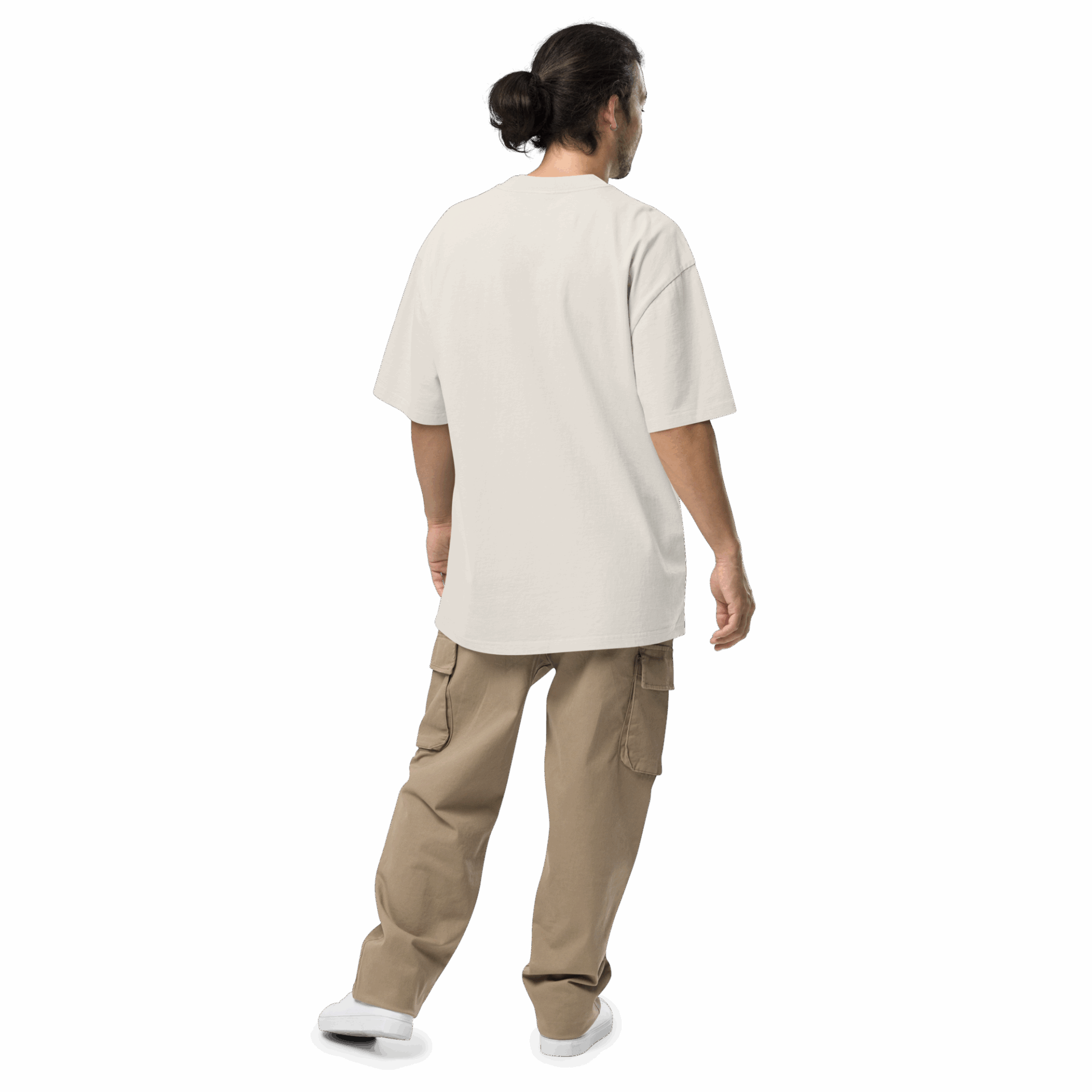 A person with long dark hair in a bun stands facing away, wearing an ADAM XXX TANTOE OUD Oversized faded t-shirt, tan cargo pants, and white shoes against a dark background.