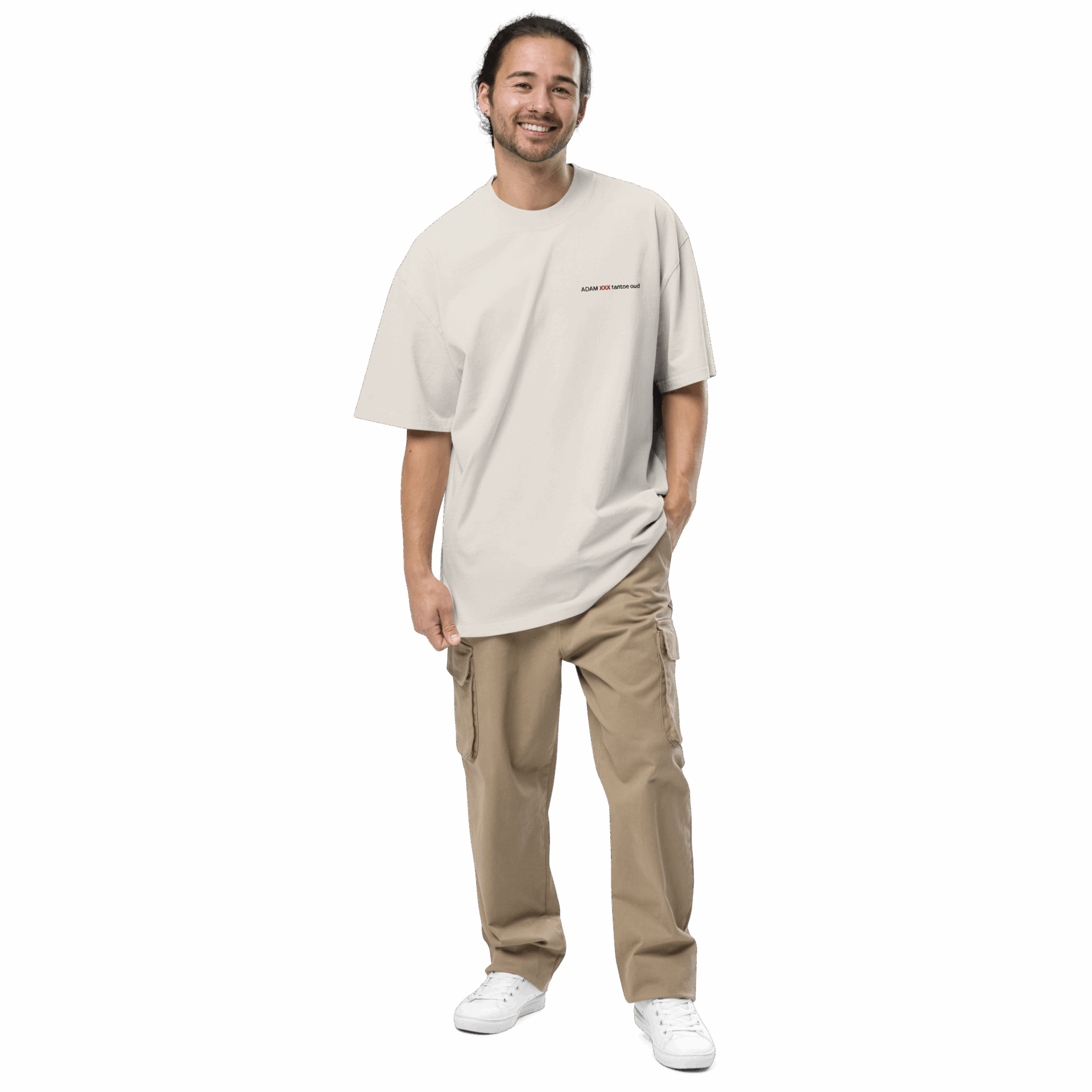 A man with long dark hair tied back is smiling and wearing an ADAM XXX TANTOE OUD Oversized faded t-shirt, khaki cargo pants, and white sneakers, standing with one hand in his pocket against a plain dark background.