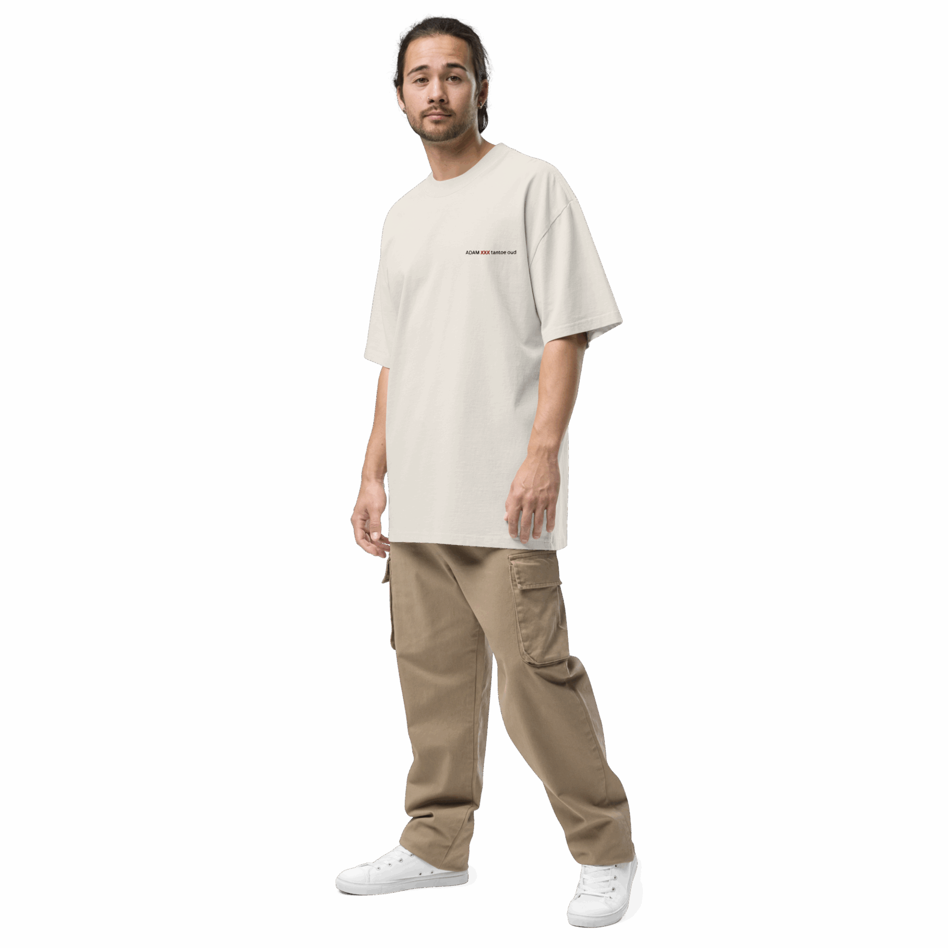 A man with long hair in a ponytail wears an ADAM XXX TANTOE OUD Oversized faded t-shirt, tan cargo pants, and white sneakers, standing against a plain black background.