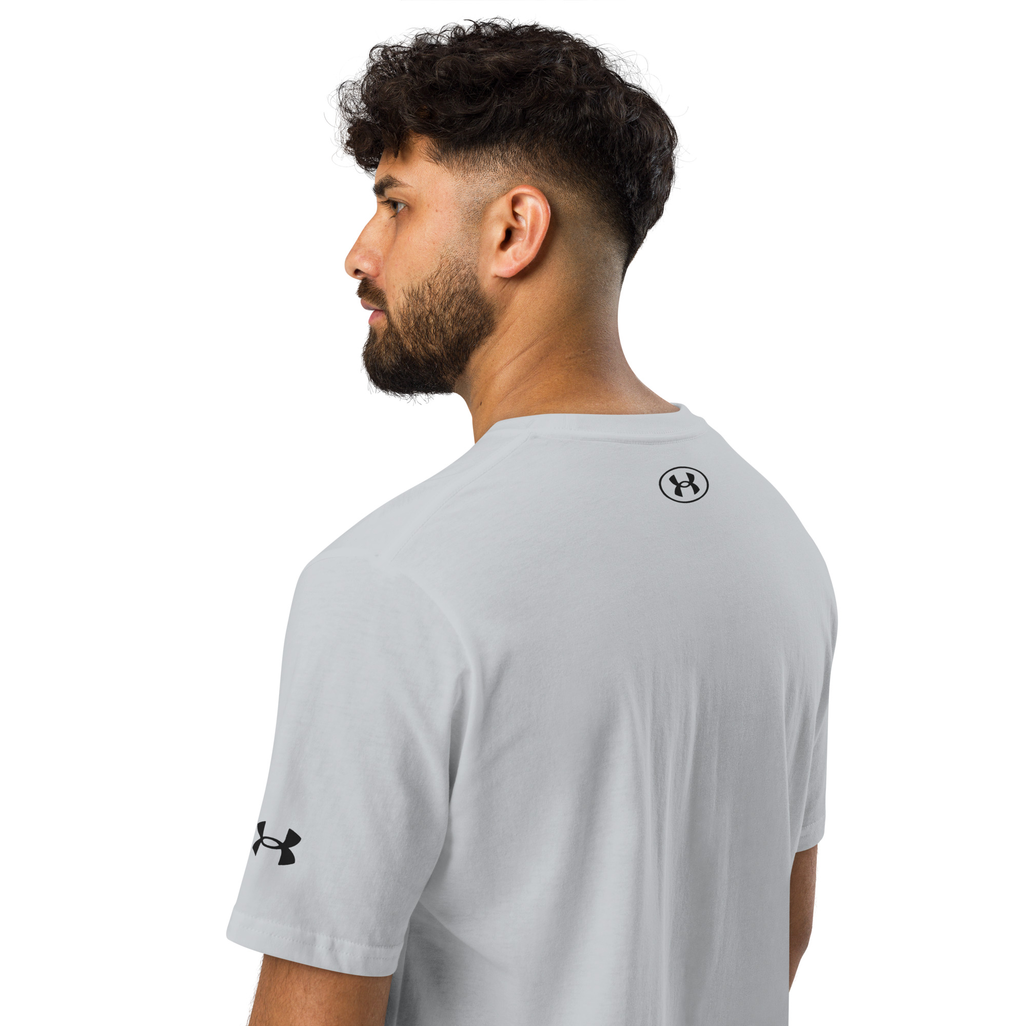 A man with short curly hair and a beard is wearing a white Under ArmourⓇ athletic t-shirt embroidered CHAMP (Copy), showing the back and side. The embroidered Under Armour logos are visible on the sleeve and upper back. A man with short curly hair and a beard is wearing a white Under ArmourⓇ athletic t-shirt embroidered CHAMP (Copy), showing the back and side. The embroidered Under Armour logos are visible on the sleeve and upper back.